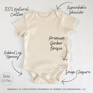 May include: Cream-colored baby onesie made of 100% natural cotton. Features include an expandable shoulder, ribbed leg opening, and snap closure. The text "Premium Gerber Onesie" is visible. The brand name "Hello Littles" is also visible.