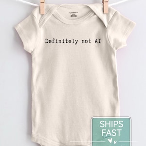 May include: A cream-colored short-sleeve baby bodysuit featuring the black text "Definitely not AI" printed across the chest. The garment has a round neckline, short sleeves, and a tag at the inner neck area with the brand name Gerber.