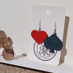 Peut inclure: Boucles d'oreilles faites à la main avec un cœur rouge et un pique bleu foncé. Les boucles d'oreilles sont présentées sur une carte blanche avec un logo. Les boucles d'oreilles sont suspendues à des crochets argentés.