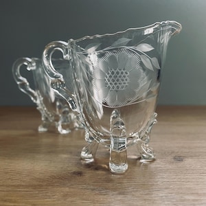 Peut inclure: Un ensemble de crémier et de sucrier en verre transparent avec des motifs floraux gravés et trois pieds.