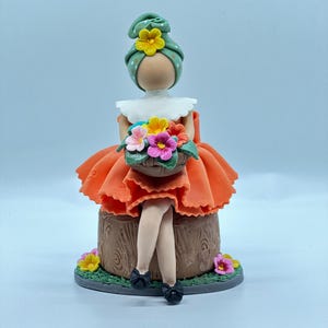 May include: A handmade doll figurine with a green headscarf, orange dress, and a basket of flowers. The doll is sitting on a brown wooden stump.