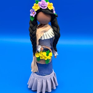 May include: A handcrafted doll with dark braids, wearing a blue dress and a floral crown. The doll carries a basket of yellow flowers and a beige scarf. The doll is approximately 6 inches tall.