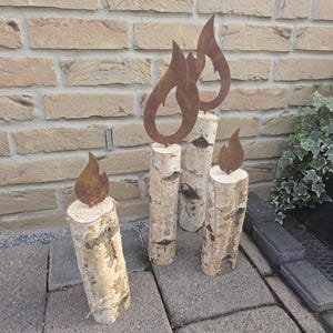 Könnte beinhalten: Vier Kerzenhalter aus Birkenholz mit rostigen Flammen-Ausschnitten aus Metall. Die Kerzenhalter sind in einer Reihe auf einer grauen Steinoberfläche angeordnet.