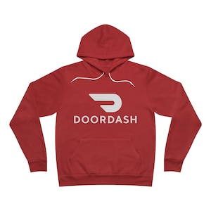 Op de afbeelding: Rode hoodie met een wit DoorDash logo en tekst. De sweatshirt heeft een capuchon met trekkoord en een voorzak. Een casual kledingstuk.