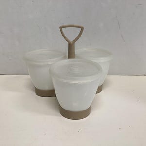 May include: A white plastic condiment server with three individual containers, each with a lid. The containers are set on a tan base and connected by a tan handle. The server is designed for easy carrying and serving.