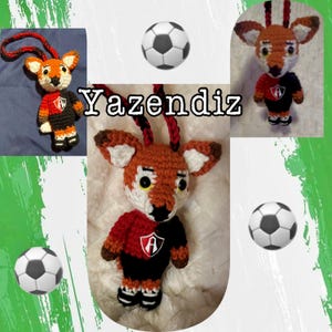 May include: Crocheted fox ornament in red, black, and orange, with a soccer ball and the word "Yazendiz". The fox is wearing a jersey with a logo. The ornament has a loop for hanging.
