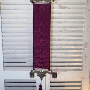Back side of Glenda Turley textile wall hanging showing burgundy fabric backing corded trim edges metal mount hardware attachment and overall construction details of vintage fiber art wall decor piece highlighting textile structure and decorative mounting design