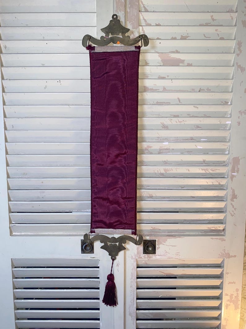 Back side of Glenda Turley textile wall hanging showing burgundy fabric backing corded trim edges metal mount hardware attachment and overall construction details of vintage fiber art wall decor piece highlighting textile structure and decorative mounting design