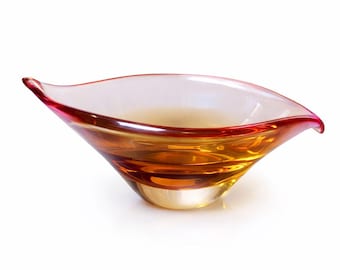 May include: A leaf-shaped glass bowl featuring a clear base that transitions into a warm amber center, finished with a vibrant red rim. The vessel has an elongated, pointed design on both ends, creating a smooth, curved silhouette throughout.