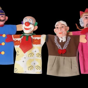 May include: Four vintage hand puppets with painted faces and fabric costumes. The puppets include a soldier in blue, a clown, an elderly woman, and a man in a pink robe. The puppets have wooden arms and are set against a black background.
