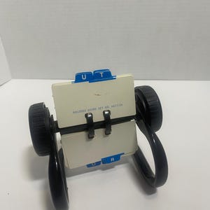 May include: A black rotary card file organizer with a rotating mechanism and two black wheels. It features off-white index cards with blue alphabetical tabs labeled U, T, O, and R. The text ROLODEX GUIDE SET NO. AG17/24 is printed on the center card.