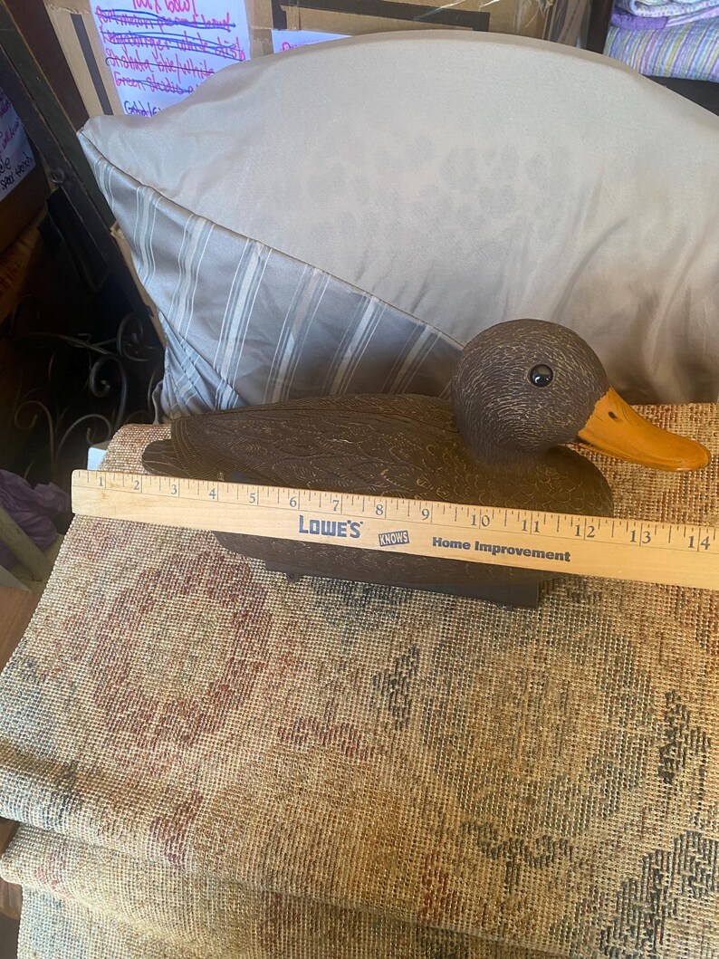 Measurement photo of hen mallard duck decoy showing approximate length around thirteen to fourteen inches using ruler, vintage Flambeau decoy size reference for waterfowl hunting or decor use, molded plastic construction with carved feather detail and natural brown tones, functional floating decoy with keel base underside, rustic cabin lodge decor styling, lake house wildlife accent, outdoorsman collectible with visible wear consistent with vintage hunting gear use