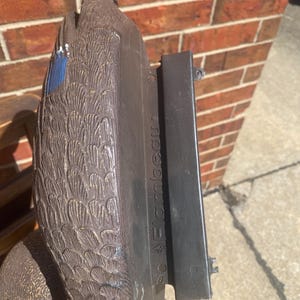 Underside view of vintage Flambeau duck decoy showing attached weighted keel base used for stability in water during hunting, molded plastic body construction visible, functional floating decoy design not intended for wall hanging, authentic waterfowl hunting gear detail, rustic sporting decor element for cabin or lodge styling, aged condition with scuffs and paint wear from outdoor use, practical decoy structure combined with collectible vintage hunting aesthetic, lake house decor inspiration
