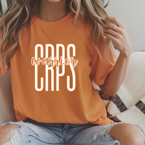May include: Orange t-shirt with white text that reads "CRPS warrior CRPS".