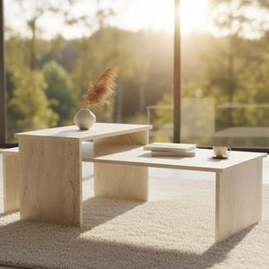 Puede incluir: Un juego de mesas de centro modernas de madera clara, con una mesa auxiliar a juego. Las mesas son rectangulares y de diseño minimalista. Un pequeño jarrón con flores secas y una taza y platillo están sobre las mesas. El conjunto está sobre una alfombra crema.