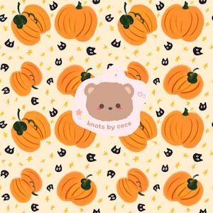 May include: A repeating pattern on a light cream background featuring orange pumpkins, small black cat faces, and yellow stars. In the centre, a light pink irregular shape displays a brown bear face and the text knots by cece.