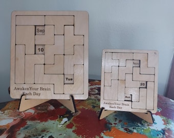 May include: Two wooden puzzle calendars, one large and one small, with the text "Awaken Your Brain Each Day." The larger calendar shows "Sep 10 Tue," and the smaller shows "Nov 20 Sun." Both are on wooden stands.