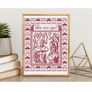 Puede incluir: Arte de punto de cruz enmarcado que representa una escena de Alicia en el país de las maravillas. El diseño en rojo y blanco incluye el texto "Who are you?" sobre los personajes. La imagen muestra una oruga sobre una seta y Alicia.