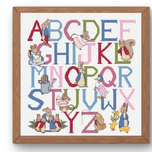 May include: Cross-stitch alphabet art in a wooden frame. Each letter is a different colour and features a character from a children's story. The text "THE TAILOR OF GLOUCESTER" is visible. The artwork is on a white background.