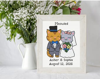 May include: A framed cross-stitch pattern featuring two cats dressed for a wedding, with the text Meowied, Asher & Sophia, and August 12, 2026. The orange cat wears a tuxedo and top hat, while the gray cat wears a white dress and veil.