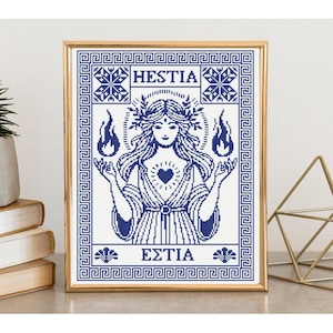 May include: A framed cross-stitch pattern featuring a blue and white design of the goddess Hestia. The artwork displays the text HESTIA and the Greek text ΕΣΤΙΑ, surrounded by a geometric Greek key border, with flames in each hand and a heart.