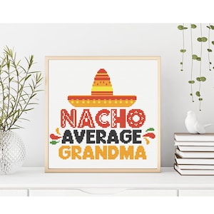 Könnte beinhalten: Ein gerahmtes Kreuzstichdesign mit den Worten "Nacho Average Grandma" in Rot, Schwarz und Orange. Ein Sombrero krönt den Text. Das Design befindet sich auf weißem Hintergrund und ist in hellbraun gerahmt.