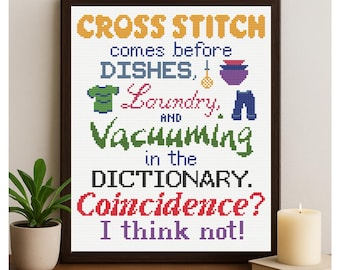 May include: A framed cross-stitch artwork featuring the text "CROSS STITCH comes before DISHES, Laundry, and Vacuuming in the DICTIONARY. Coincidence? I think not!" The text is in multiple colours, with stitched images of a shirt, dishes, and trousers.