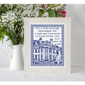 May include: A framed cross-stitch artwork with a quote in blue and white. The quote reads, "It is a truth universally acknowledged, that a single man in possession of a good fortune, must be in want of a wife."