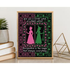 Puede incluir: Obra de arte de punto de cruz enmarcada con un marco dorado. La obra presenta una princesa rosa y una bruja verde, con el texto "Are you a GOOD witch or a BAD witch?" y "Perspective is the magic that changes everything."