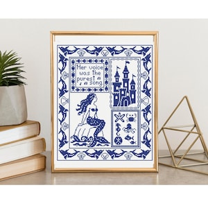 Puede incluir: Arte de punto de cruz enmarcado que presenta una sirena, un castillo y criaturas marinas en tonos azules. El texto dice: "Her voice was the purest song". La obra de arte se muestra en un marco dorado.