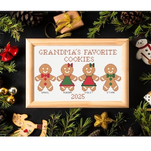 May include: A framed cross-stitch embroidery featuring the text GRANDMA'S FAVORITE COOKIES above four gingerbread figures with names Daniel, Aurora, Violet, and Ethan, and the year 2025. The figures wear red and green accents.