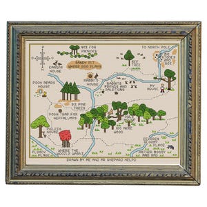 May include: Cross-stitch map depicting a whimsical forest with landmarks such as Rabbit's House, Piglet's House, and the North Pole. The map is framed in a gold-coloured frame with a green and blue border. The text "Drawn by Me and Mr Shepard Helpd" is at the bottom.