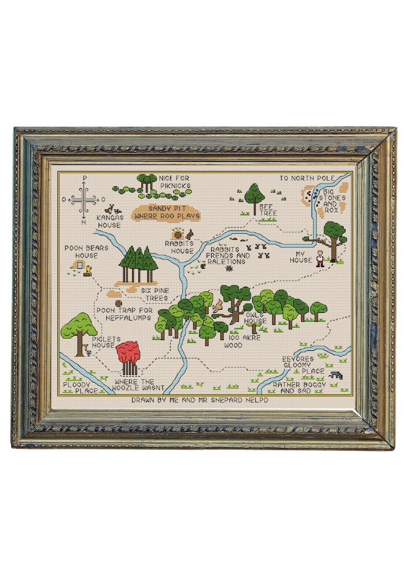 May include: Cross-stitch map of a whimsical forest with landmarks like Rabbit's House, Piglet's House, and the North Pole. The map is framed in a gold-colored frame with a green and blue border. The text "Drawn by Me and Mr Shepard Helpd" is at the bottom.