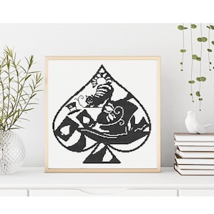 Può includere: Uno schema a punto croce incorniciato di forma quadrata con una figura di picche nera su sfondo bianco. All'interno della picca, un dettagliato design a silhouette raffigura un gatto, un cilindro, carte da gioco ed elementi floreali.