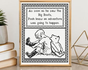 May include: A framed cross-stitch pattern featuring a black and white illustration of a child putting on boots next to a bear. The text reads: As soon as he saw the Big Boots, Pooh knew an adventure was going to happen. The design has a geometric border.