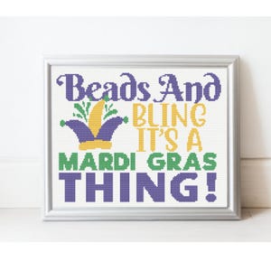 Peut inclure: Une œuvre d'art au point de croix encadrée avec les mots "Beads And Bling It's A Mardi Gras Thing!" en violet, vert et jaune. L'œuvre présente un motif de chapeau de bouffon violet, jaune et vert.