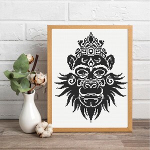 Puede incluir: Un patrón de punto de cruz enmarcado que presenta una ilustración gráfica en blanco y negro de una cabeza de gorila con detalles geométricos simétricos y un diseño en forma de corona, en un marco de madera clara.