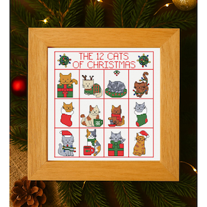 Puede incluir: Un bordado a punto de cruz enmarcado con la frase "THE 12 CATS OF CHRISTMAS" y doce ilustraciones de gatos. Cada gato está en una escena navideña, como dentro de una caja de regalo o con un gorro de Papá Noel. El marco es de madera clara.