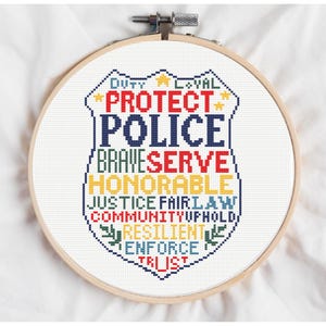 Puede incluir: Un diseño de punto de cruz en un aro de madera. El diseño presenta una forma de insignia de policía con las palabras "Protect Police Brave Serve Honorable Justice Fair Law Community Uphold Resilient Enforce Trust".