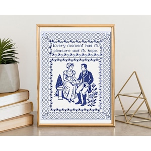 May include: Framed cross-stitch art with a gold frame. The artwork features a blue and white design of a couple and the quote, "Every moment had its pleasure and its hope." The frame is displayed on a wooden surface.