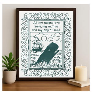 Puede incluir: Arte de punto de cruz en un marco de madera oscura. La obra presenta una ballena rompiendo el océano, un barco y el texto "All my means are sane, my motive and my object mad." El diseño es en tonos turquesa y blanco.