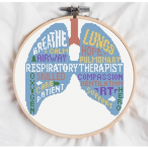 Puede incluir: Bordado de punto de cruz en un aro de madera con un diseño de pulmón azul con palabras como "Respirar", "Vía aérea" y "Terapeuta respiratorio". El diseño incluye varios colores y está sobre un fondo blanco.