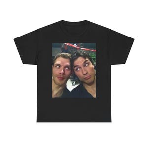 Op de afbeelding: Zwart t-shirt met een foto van twee mannen met gekruiste ogen en grappige gezichtsuitdrukkingen. De afbeelding staat centraal op het shirt en benadrukt het ontwerp. Het t-shirt is gemaakt van zacht materiaal.