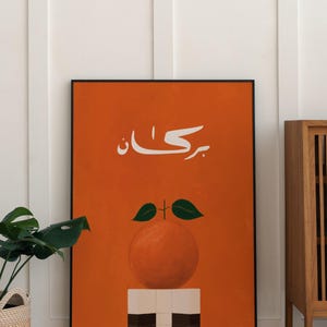 Puede incluir: Impresión artística de color naranja con texto árabe. La obra presenta una naranja estilizada con hojas verdes, sobre un fondo naranja liso. La impresión está enmarcada en negro y se exhibe en interiores.