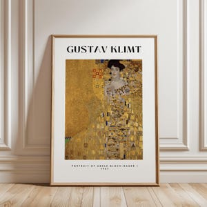 May include: A framed print of Gustav Klimt's "Portrait of Adele Bloch-Bauer I" from 1907. The artwork features a woman in a gold dress with intricate patterns. The print is in a gold frame and is displayed against a white wall.