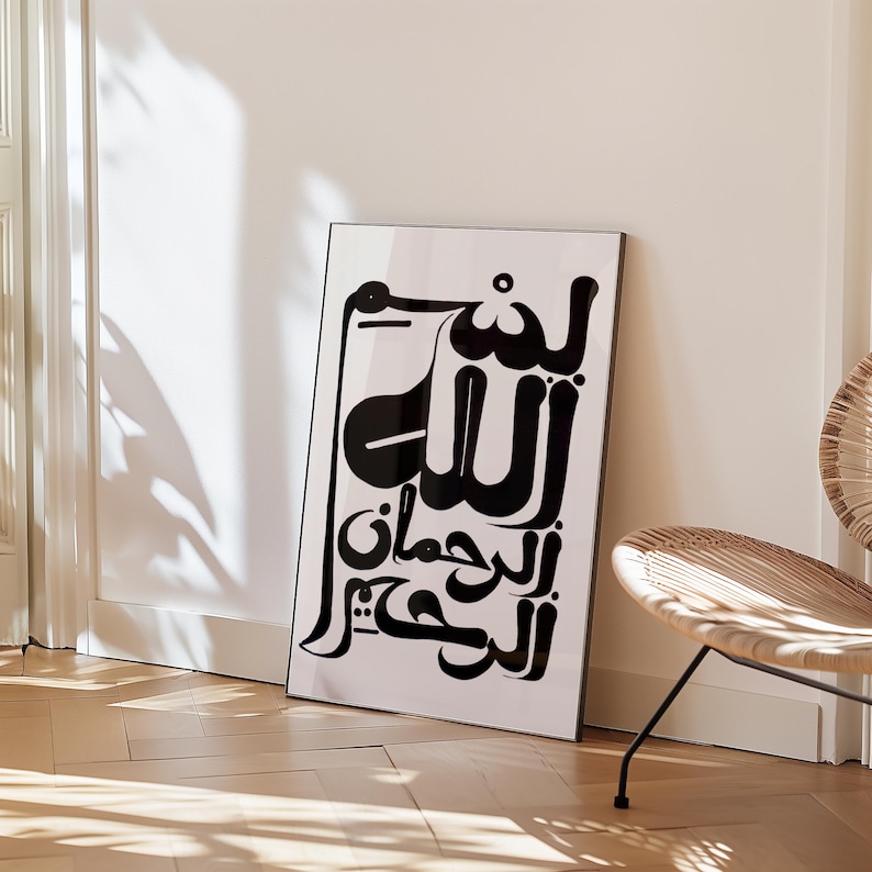 Black and white framed art print featuring Arabic calligraphy. The artwork displays elegant script on a white background, set within a sleek black frame. The print is leaning against a white wall, with a wooden floor in the foreground.