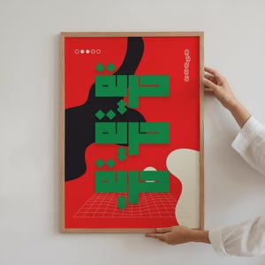 Könnte beinhalten: Ein gerahmter Kunstdruck mit rotem Hintergrund, grüner arabischer Kalligraphie und abstrakten schwarzen und weißen Formen. Der Druck hat einen Holzrahmen und wird von einer Person gehalten.