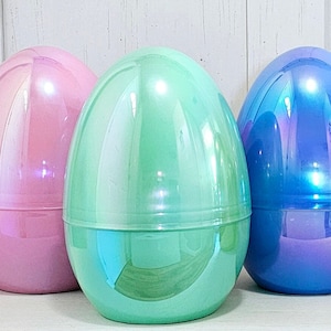 May include: Five large, iridescent Easter egg containers in shades of pink, green, blue, gold, and teal. Each egg is two-piece, with a base and a top, and has a glossy, reflective surface. The eggs are arranged in a row, suggesting a festive theme.