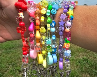 May include: A set of eight colorful beaded keychains with different charms, including hearts, flowers, smiley faces, and fruit. Each keychain has a silver metal clasp.
