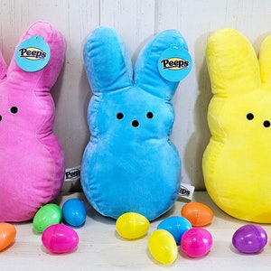 May include: Three plush Peeps bunny toys in pink, blue, and yellow. Each bunny has a tag that says "Peeps" and is surrounded by plastic Easter eggs in various colors.